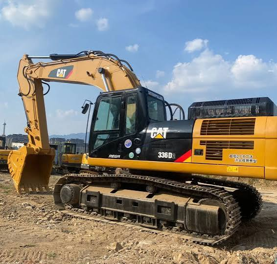 Yellow and black tracked excavator parked on a dirt lot under a blue sky